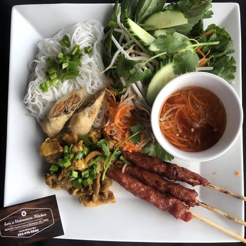 A Vietnamese dish with noodles, spring rolls, grilled skewers, and a side salad with dressing.