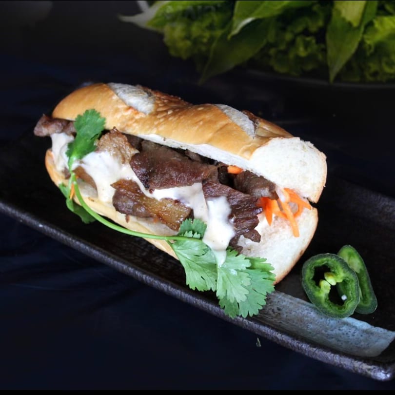 A Vietnamese banh mi sandwich with beef, cilantro, and sauce, served with jalapeño slices.